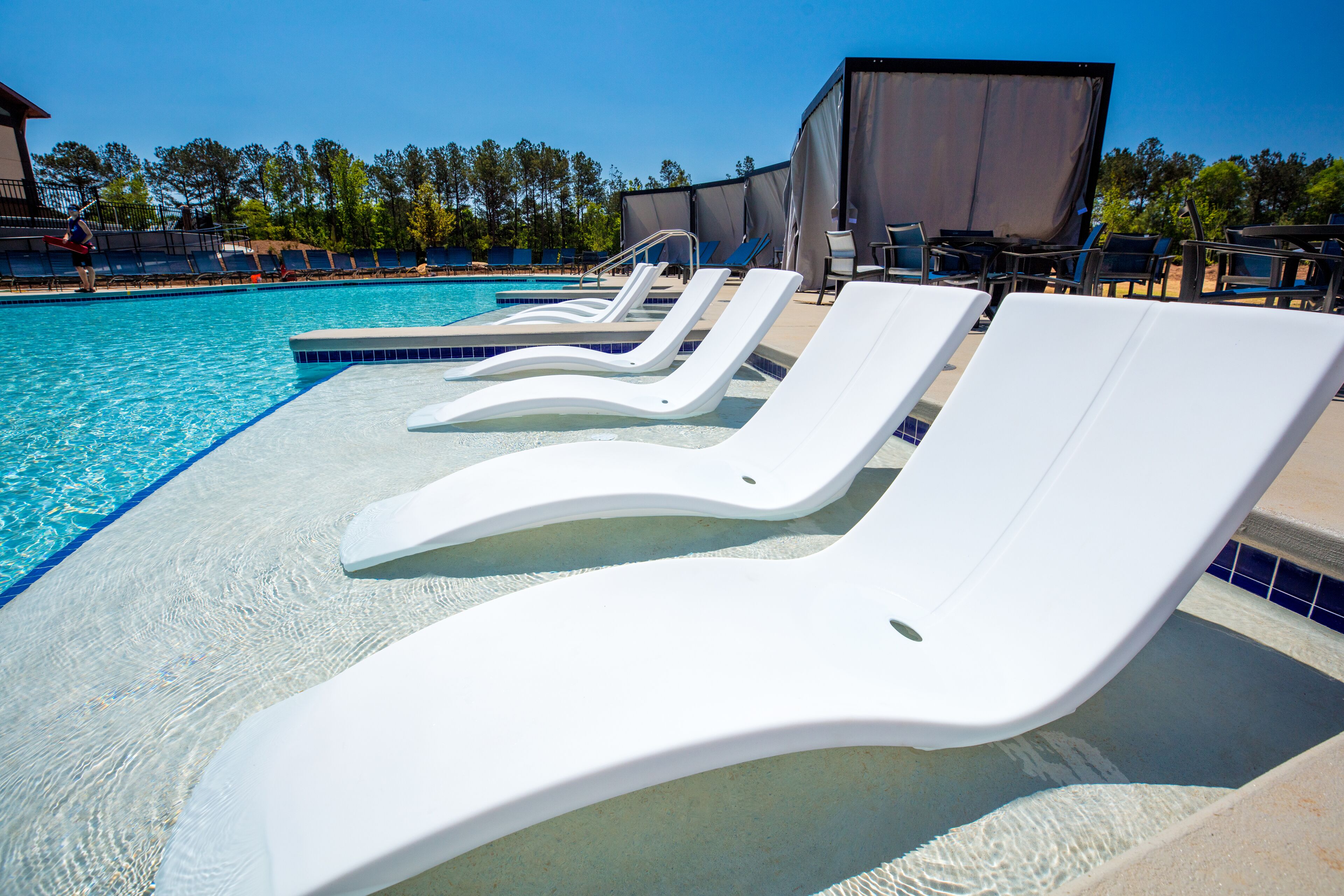A pool with white lounge chairs and a covered area.