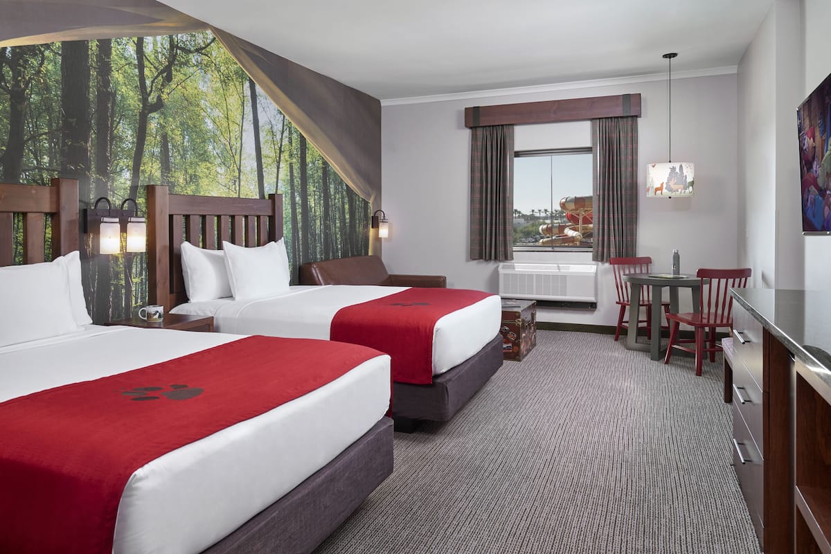 Habitación de hotel con dos camas, un escritorio y vista a un parque acuático.
