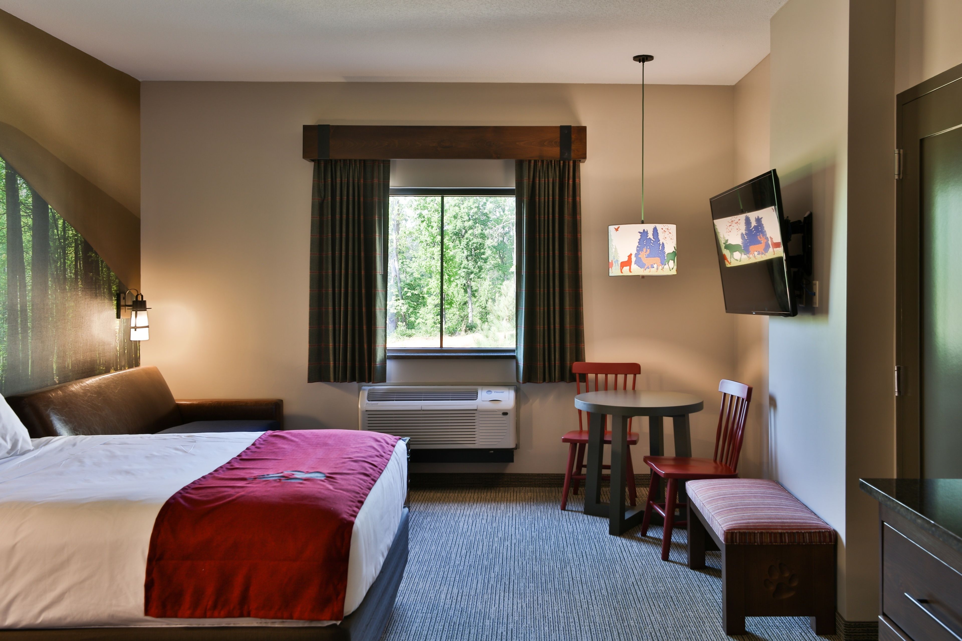 Habitación de hotel con cama, escritorio, silla, banco, televisor y ventana con cortinas.