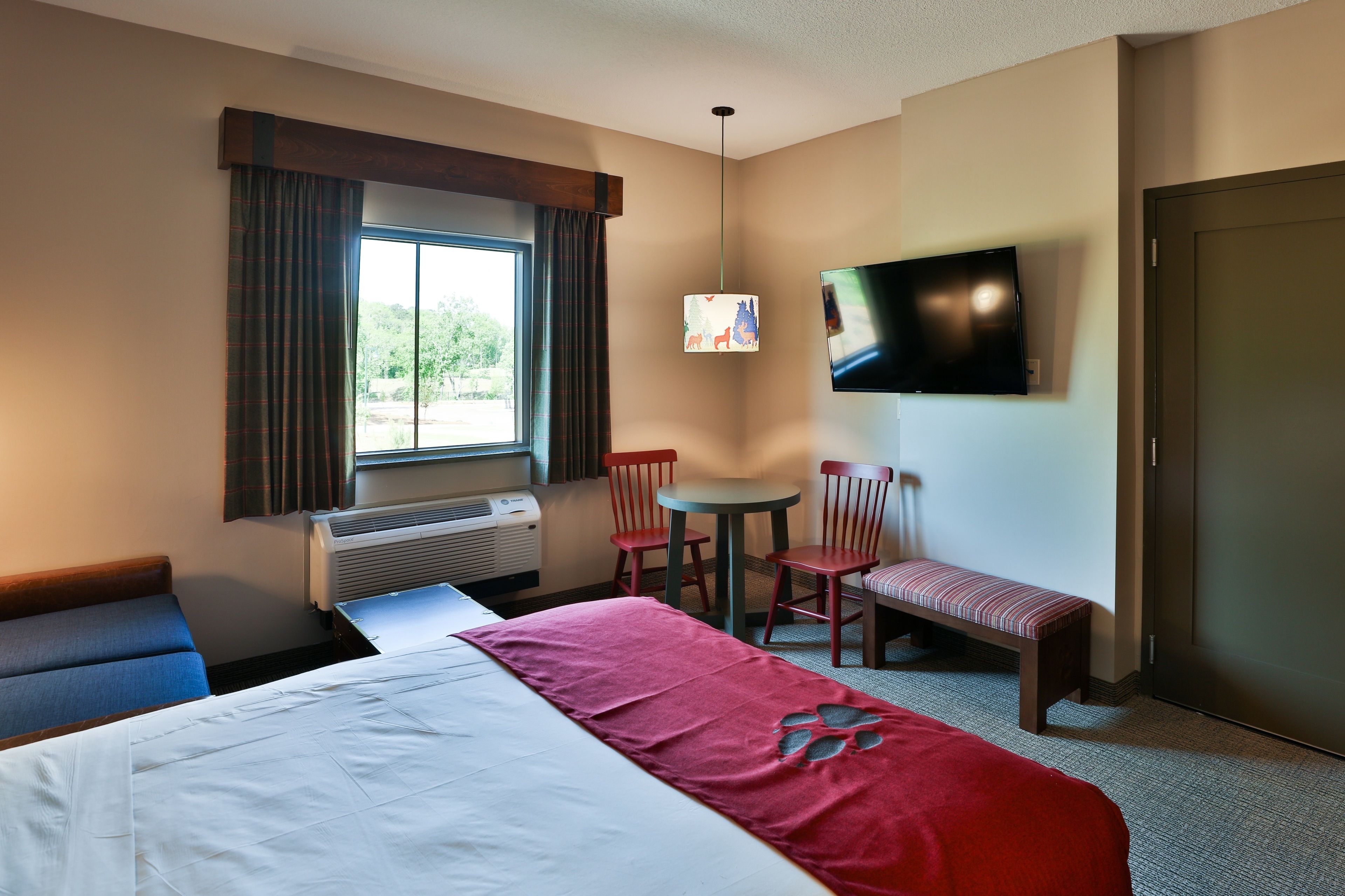 A hotel room with a bed, a desk, a chair, a bench, a TV, and a window with curtains.