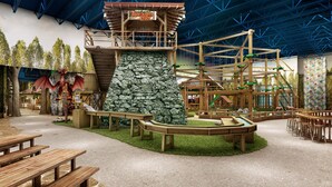 Un espace de jeux avec des structures d’escalade, une tour en bois et des tables de pique-nique.