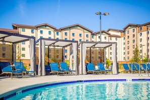 A swimming pool with lounge chairs and a covered seating area, surrounded by multi-story buildings. - Great Wolf Lodge Atlanta / LaGrange, GA (LaGrange)