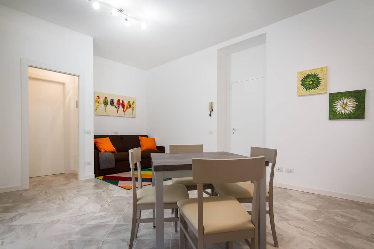 Ein Essbereich mit Tisch und Stühlen, einer Couch mit Kissen und einem farbenfrohen Teppich.