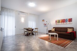 A modern living room with a brown sofa, a dining table with chairs, and a colorful abstract painting on the wall. - Benzi (Como)