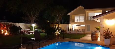 A swimming pool with a tiled edge, surrounded by outdoor furniture and a well-lit patio area.