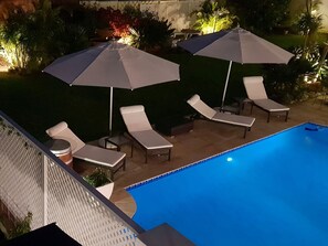 Ein Poolbereich mit Liegestühlen, Sonnenschirmen und einem gepflegten Garten.