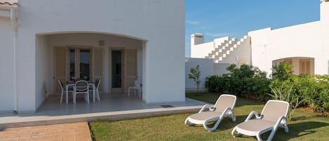 A modern outdoor area with a patio, two lounge chairs, a table with chairs, and a small garden.