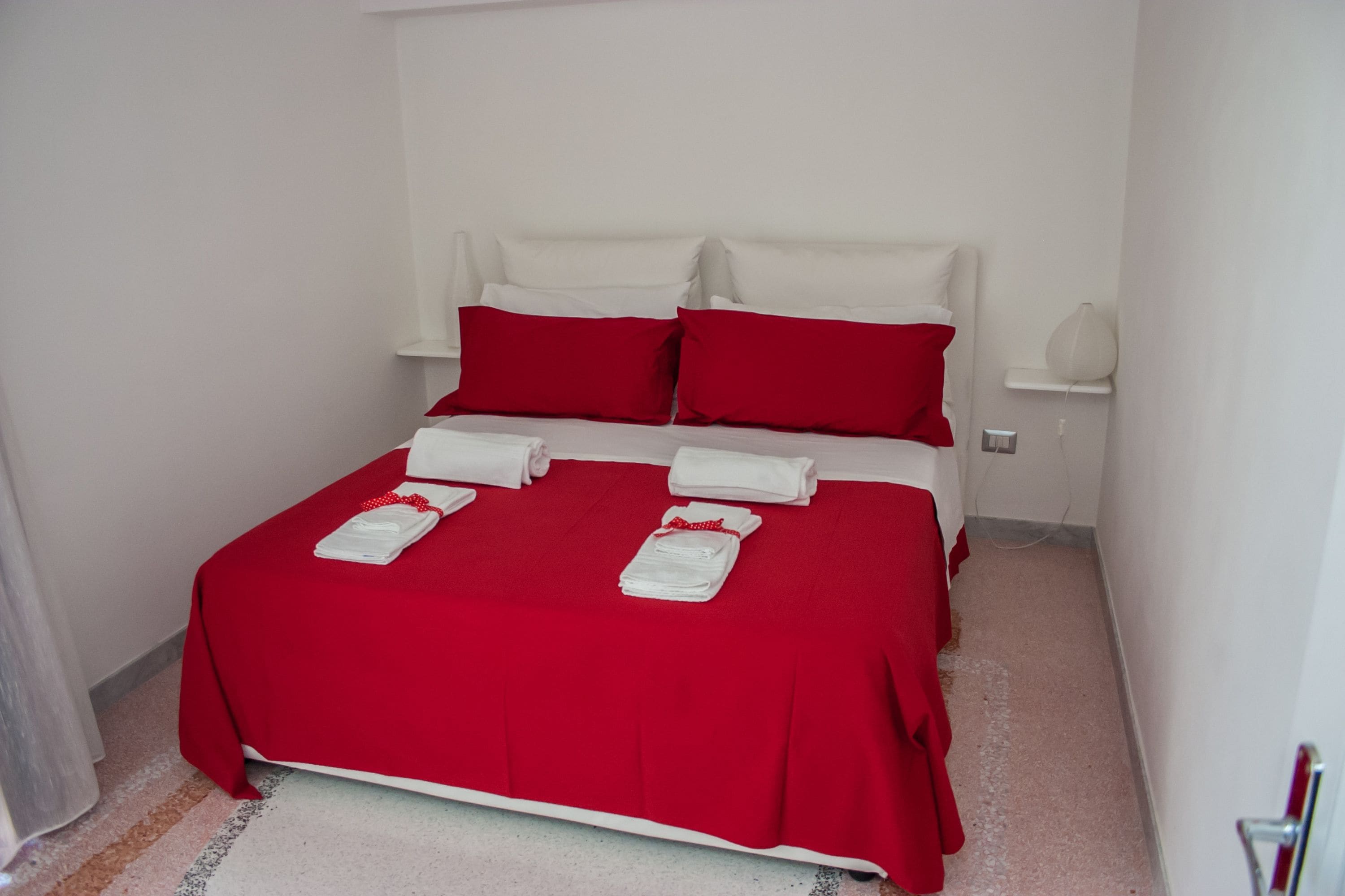 A neatly made bed with a red bedspread, white pillows, and folded white towels.