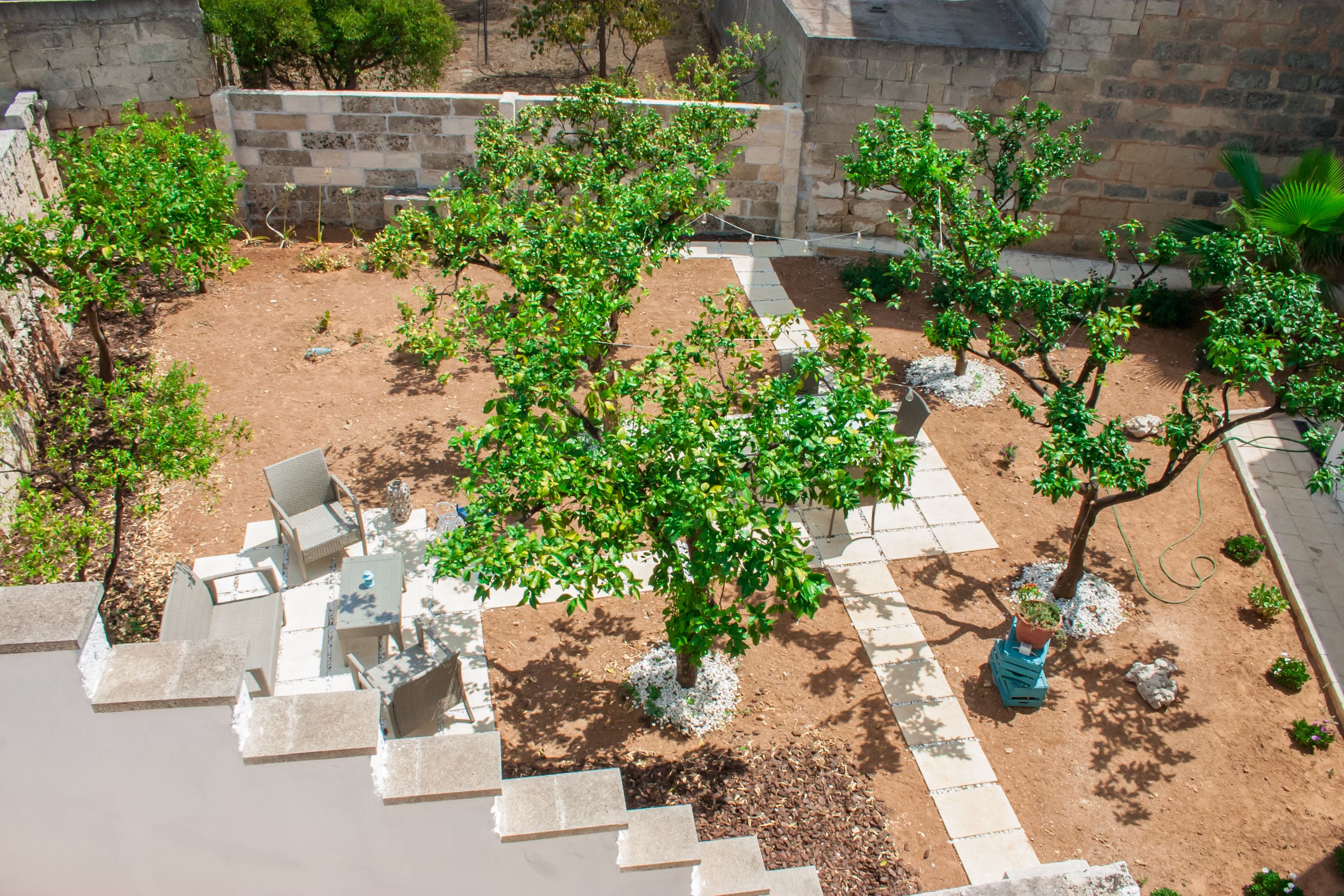 A courtyard with a stone wall, a tree, and a seating area with chairs and a table.