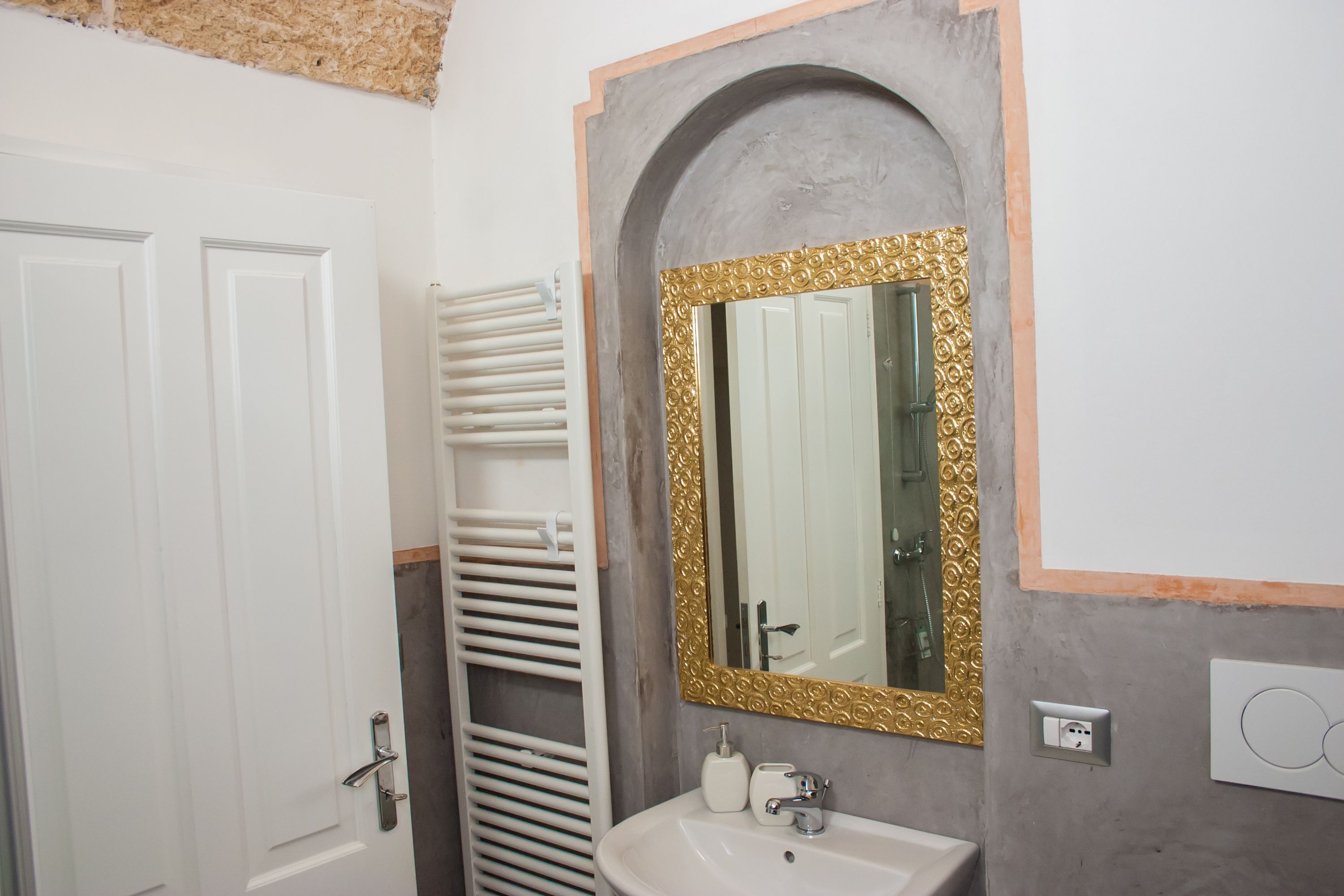 Un bany amb una porta blanca, una barra de tovalloles blanca, un lavabo amb mirall daurat i un dispensador de tovalloles.