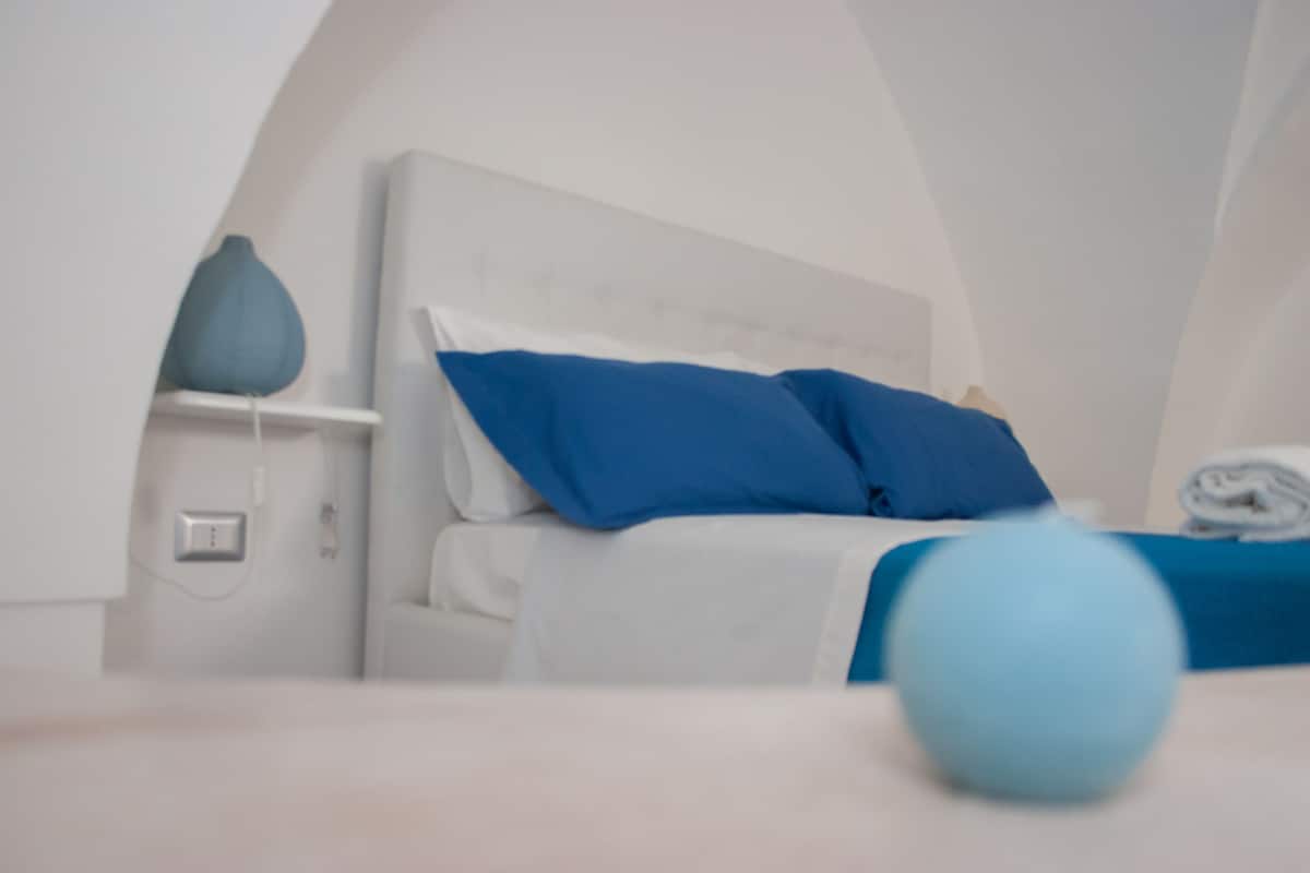 Une chambre à coucher moderne avec un lit blanc, des oreillers bleus et un vase bleu posé sur la table de chevet.