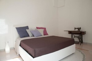 A bedroom with a bed, pillows, a desk with a sewing machine, and a white wall. - Riz Salento Guest House (Montesano Salentino)