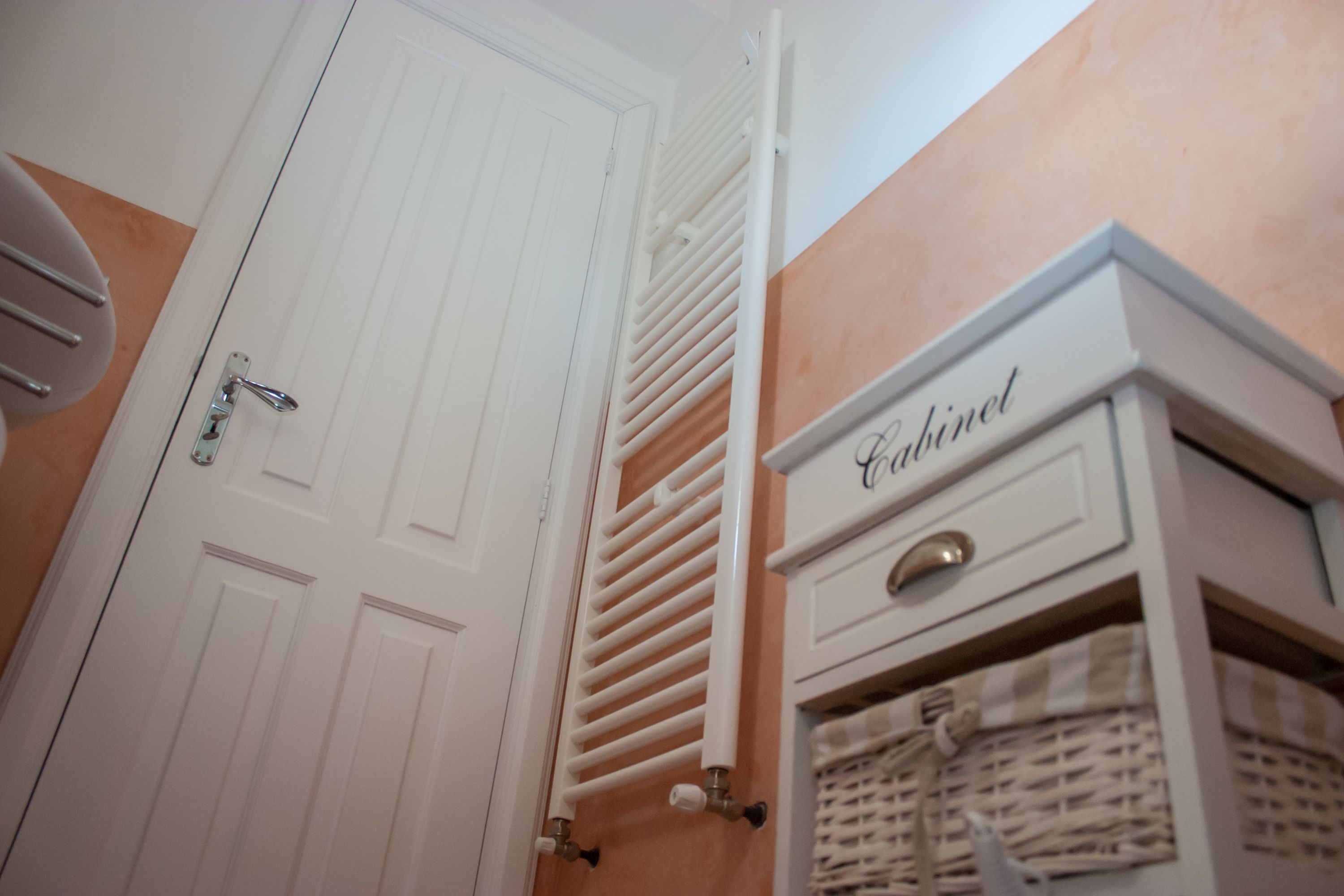 A white door with a silver handle, a white radiator, and a cabinet labeled "Cabinet" with wicker baskets.
