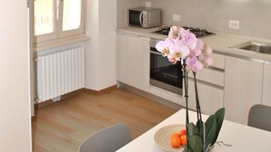 Une cuisine moderne avec des meubles blancs, un four à micro-ondes et une cuisinière à gaz. On y trouve une table à manger ornée d’un vase de fleurs et d’un verre d’eau.