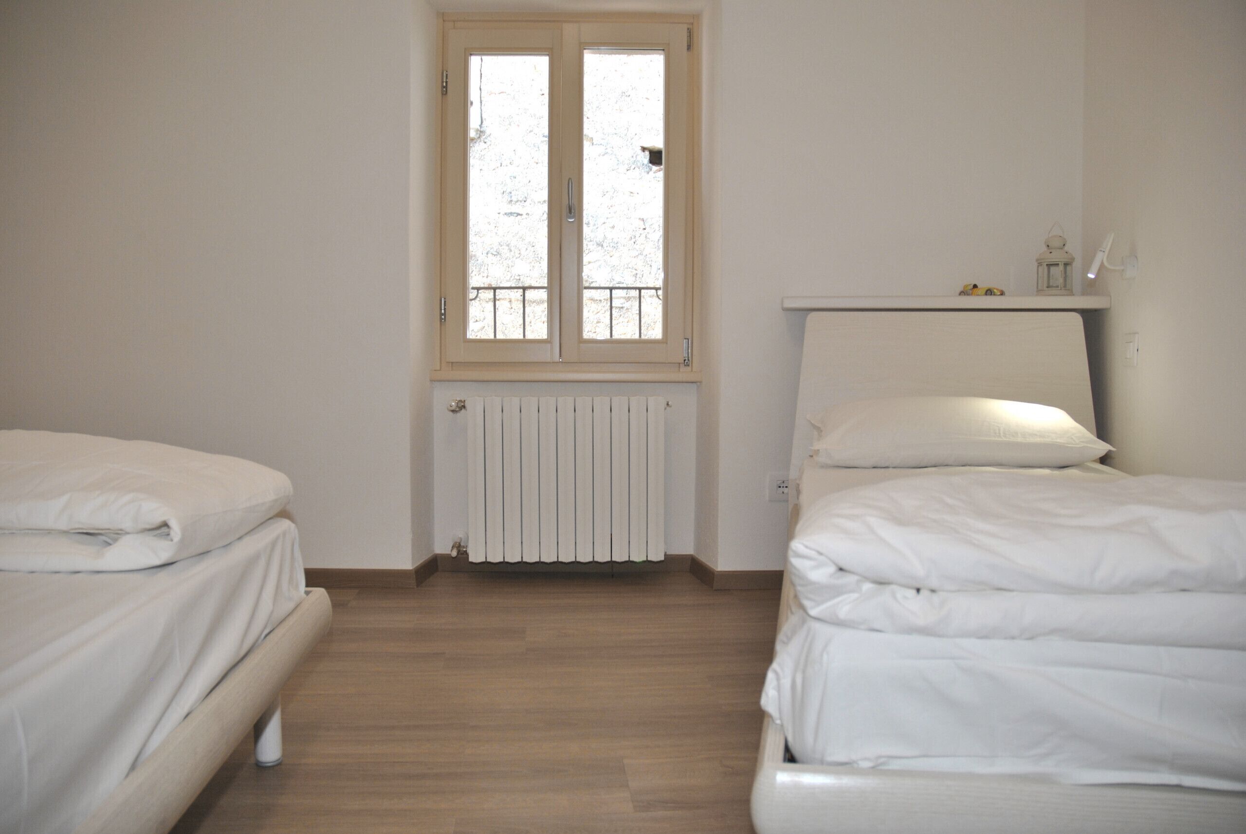 Une chambre avec deux lits, un radiateur, une fenêtre et une étagère sur laquelle se trouve une lanterne.