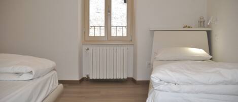 Une chambre avec deux lits, un radiateur, une fenêtre et une étagère sur laquelle se trouve une lanterne.