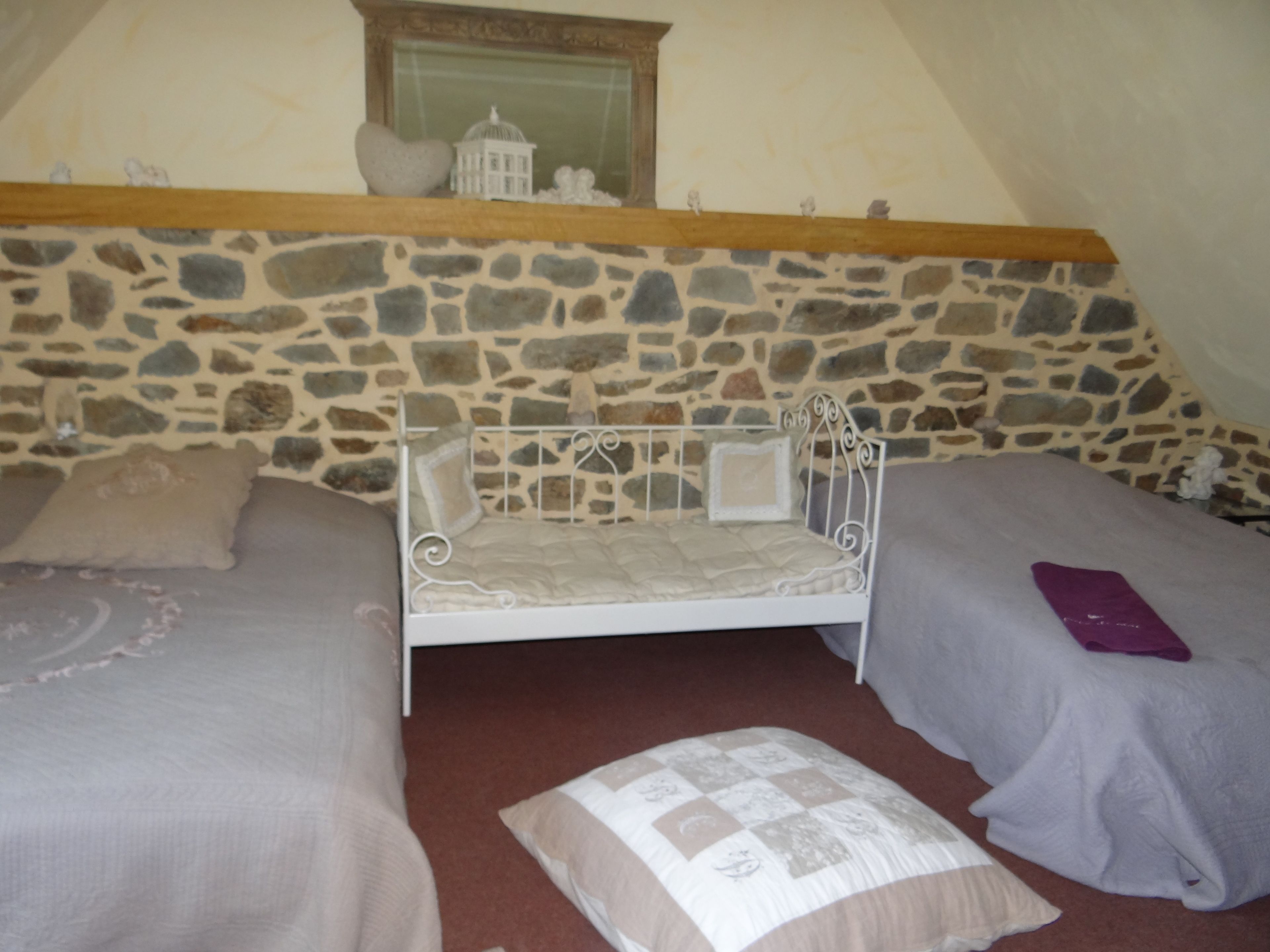 Une chambre avec un mur en pierre, un lit, deux oreillers et une table de chevet.