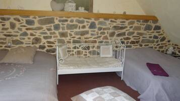 Une chambre avec un mur en pierre, un lit, deux oreillers et une table de chevet.