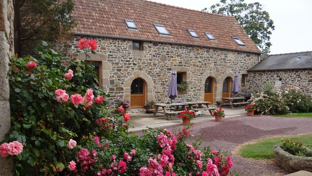 A stone building with a tiled roof, outdoor seating, and blooming pink flowers. - Ecuries de Kerbalan Gîtes à la ferme (Gommenec'h)