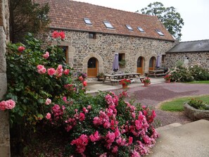 Edificio de piedra con tejado de tejas, mesas al aire libre y flores rosadas en flor.