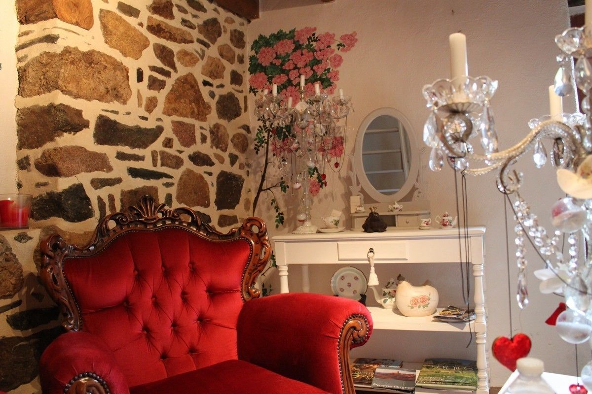 A red upholstered armchair, a stone wall, a chandelier, and a white dresser with various items.