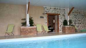 An indoor swimming pool with a stone wall, green lounge chairs, and potted plants. - Ecuries de Kerbalan Gîtes à la ferme (Gommenec'h)
