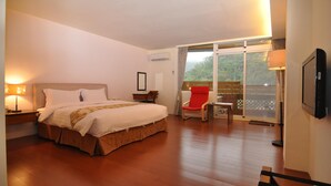Un dormitorio con una cama grande, una silla roja, un televisor y un balcón con terraza de madera.