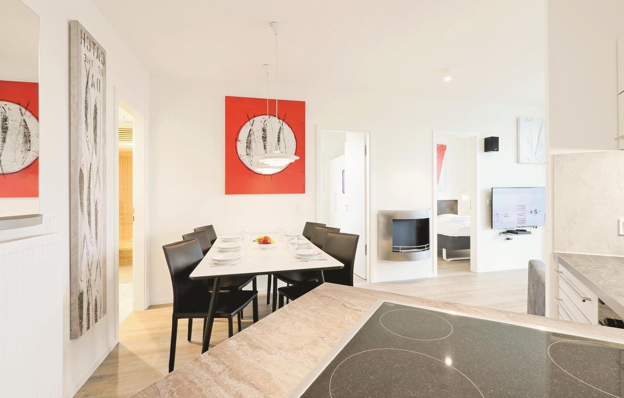 A modern kitchen with a large island, a dining area with a white table and black chairs, and a living area with a TV and seating.