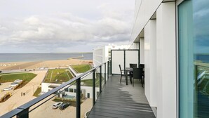 Ein Balkon mit Blick auf Strand und Meer, inklusive Tisch und Stühlen, sowie ein Parkplatz mit Autos.