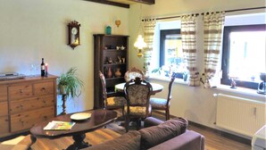 A cozy living room with a wooden ceiling, a dining table with chairs, a bookshelf, and a window with curtains. - Müller's Landidyll - Apartments Müller's Landidyll (Klitten)