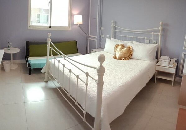 A neatly arranged bedroom with a white bed, green sofa, and a small table.