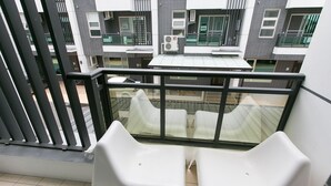 A balcony with two white plastic chairs, a glass railing, and a view of a multi-story building with air conditioning units. - Love 300 (Luodong)