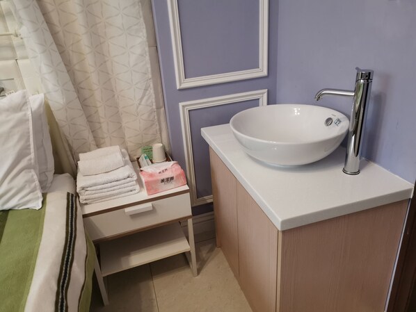 A bathroom with a white sink, a towel rack with folded towels, a small table with toiletries, and a shower curtain. - Love 300 (Luodong)