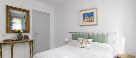A bedroom with a bed, a bedside table, a dresser, a mirror, and a painting on the wall.