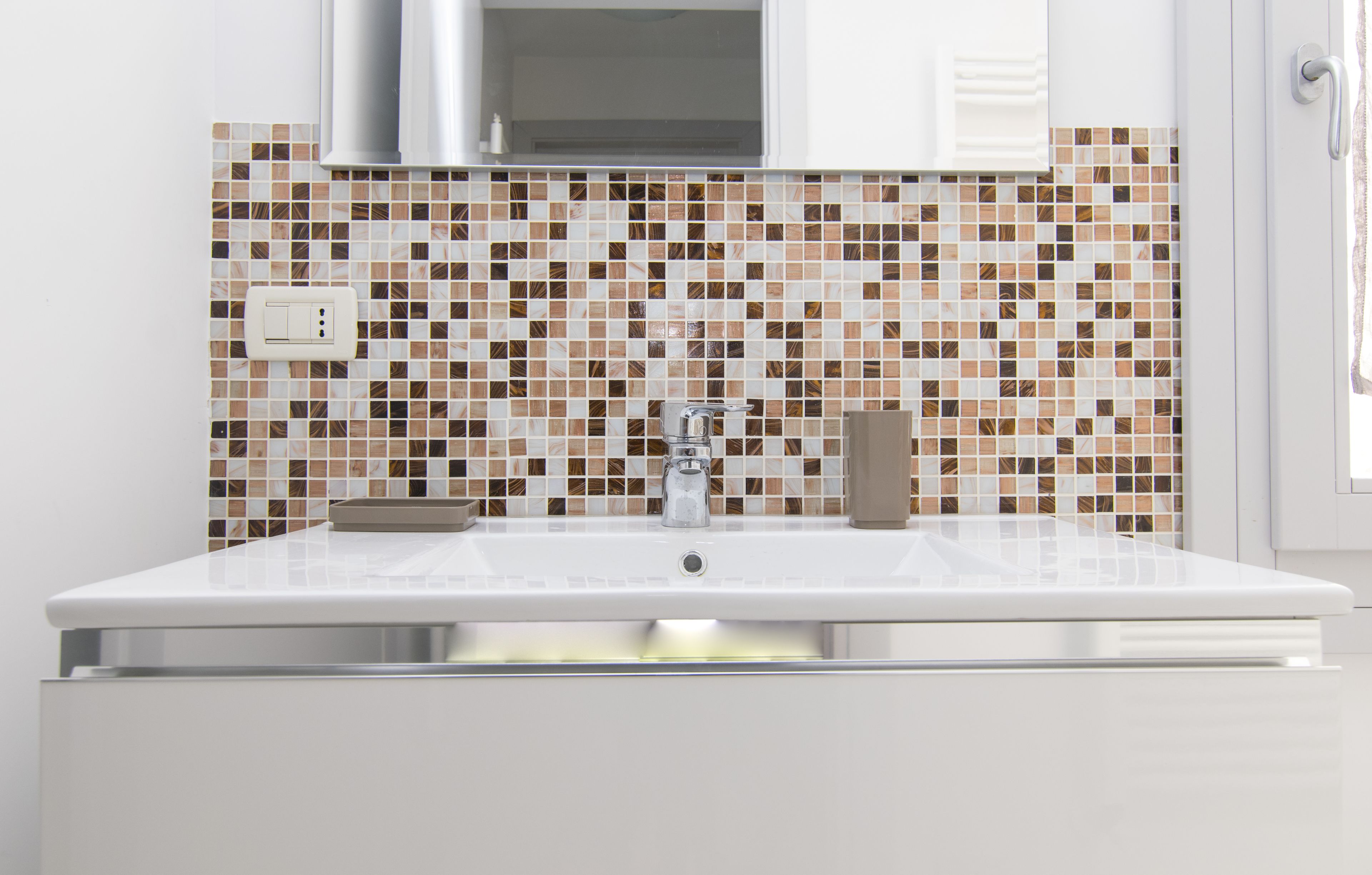 A bathroom with a white sink, a modern faucet, and a tiled backsplash.