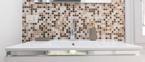 A bathroom with a white sink, a modern faucet, and a tiled backsplash.