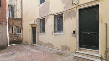 Un estrecho callejón con pavimento de ladrillo, un edificio con pintura descascarada, ventanas con barrotes y una puerta cerrada.
