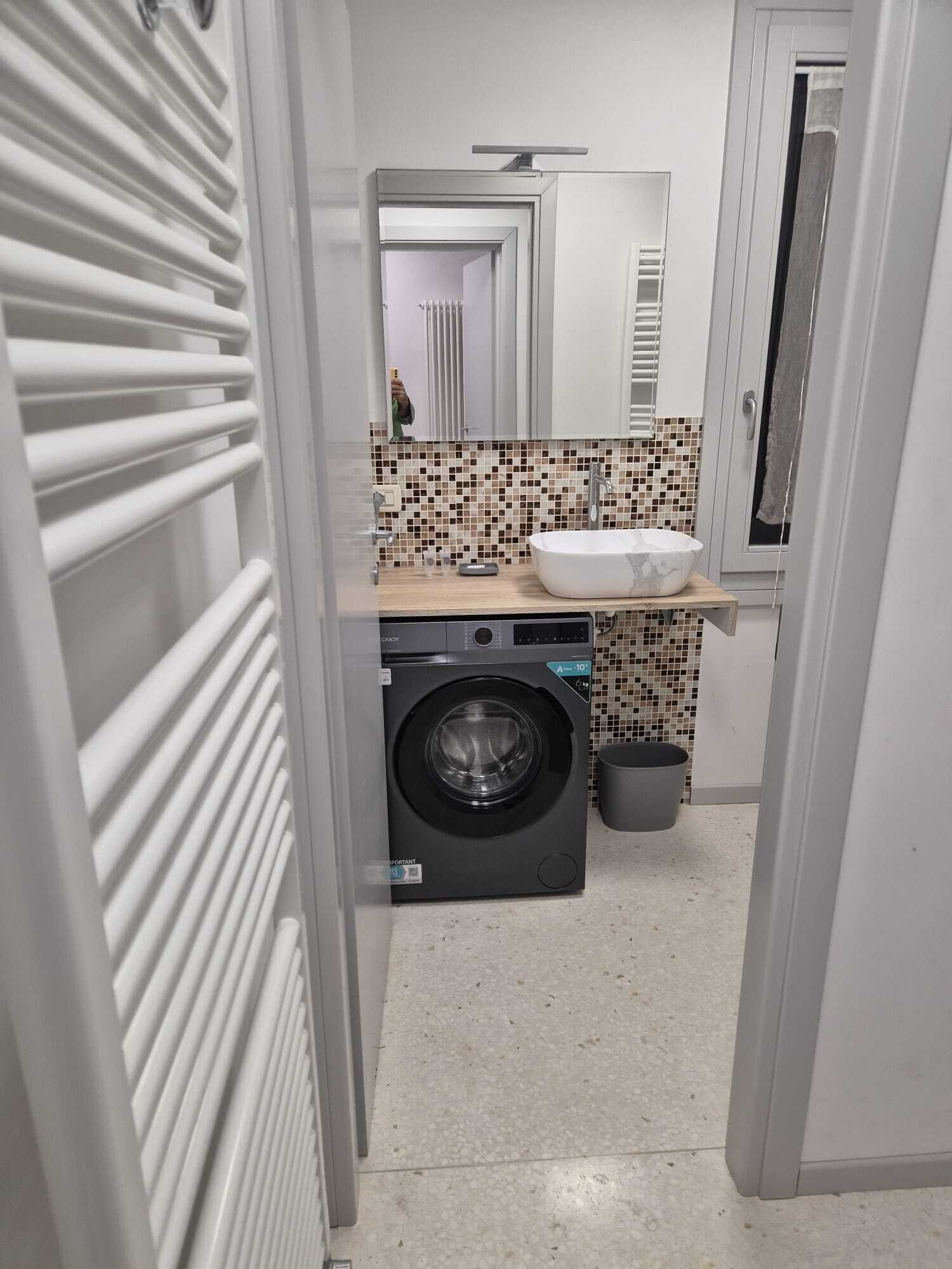 A compact bathroom with a washing machine, a sink, and a tiled backsplash.