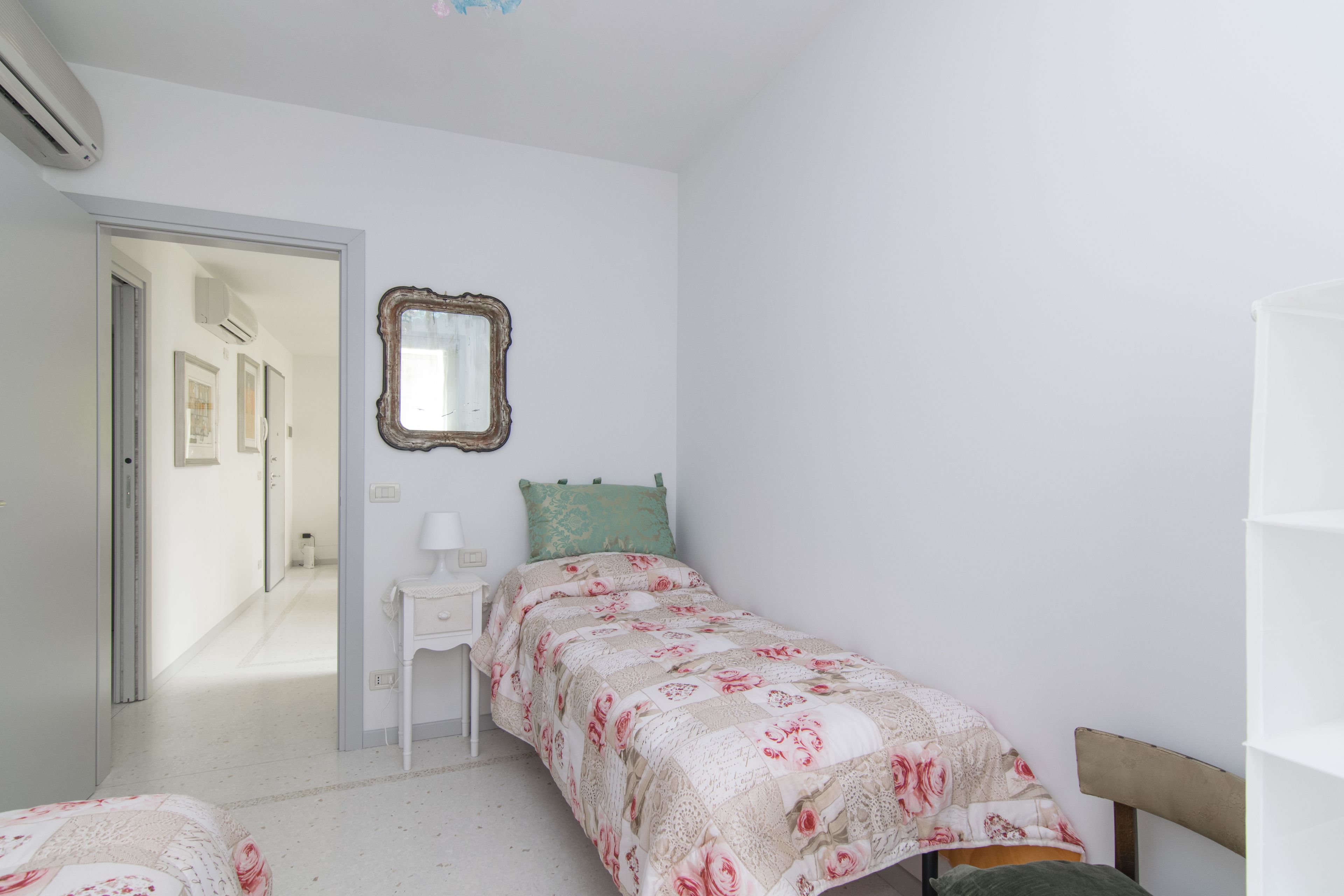 A bedroom with a bed, a nightstand, a mirror, and a door leading to another room.