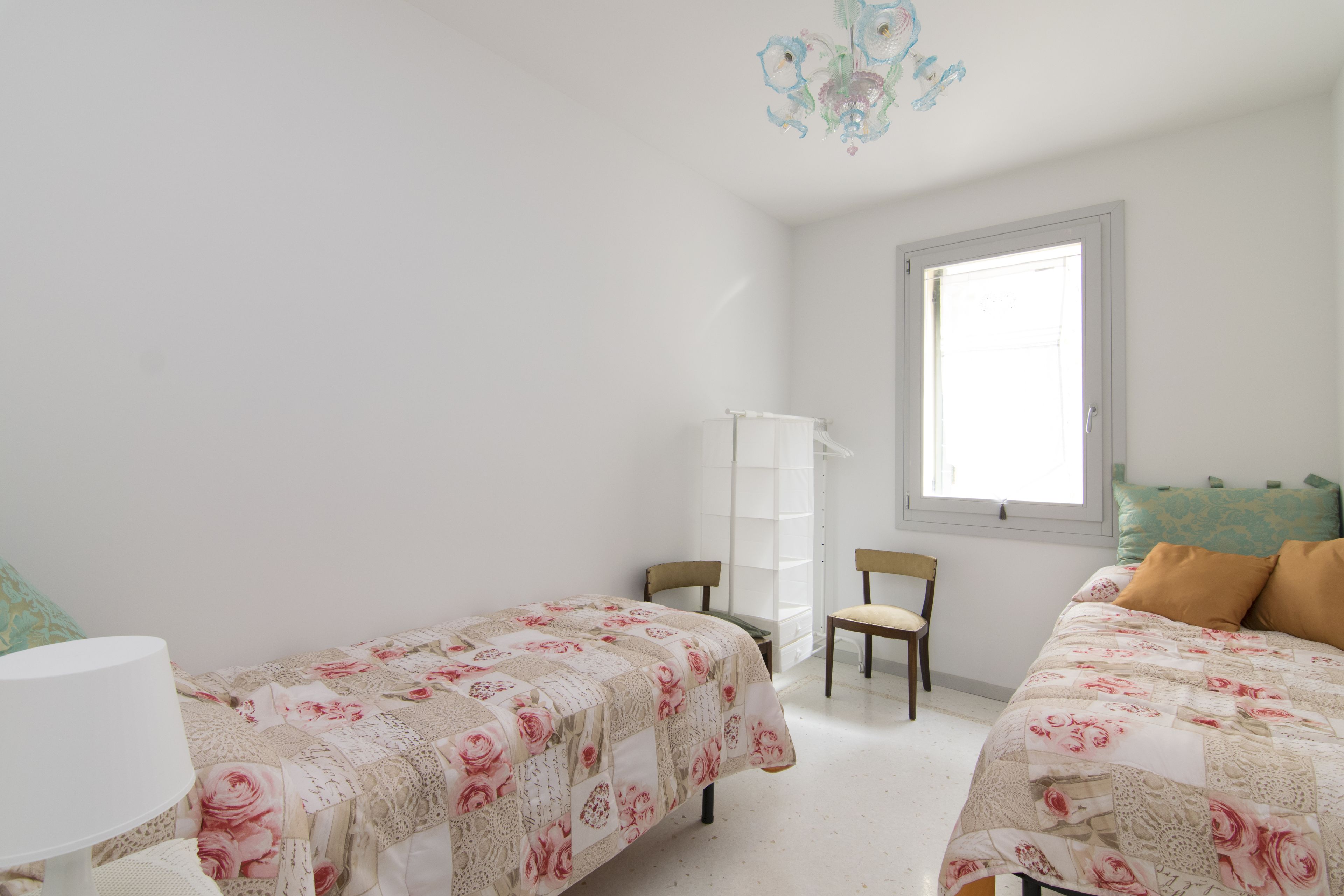 A bedroom with two beds, a window, and a chandelier.