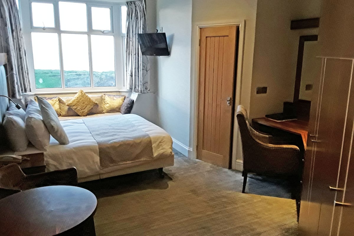 A bedroom with a bed, a desk, a chair, a TV mounted on the wall, and a window with curtains.
