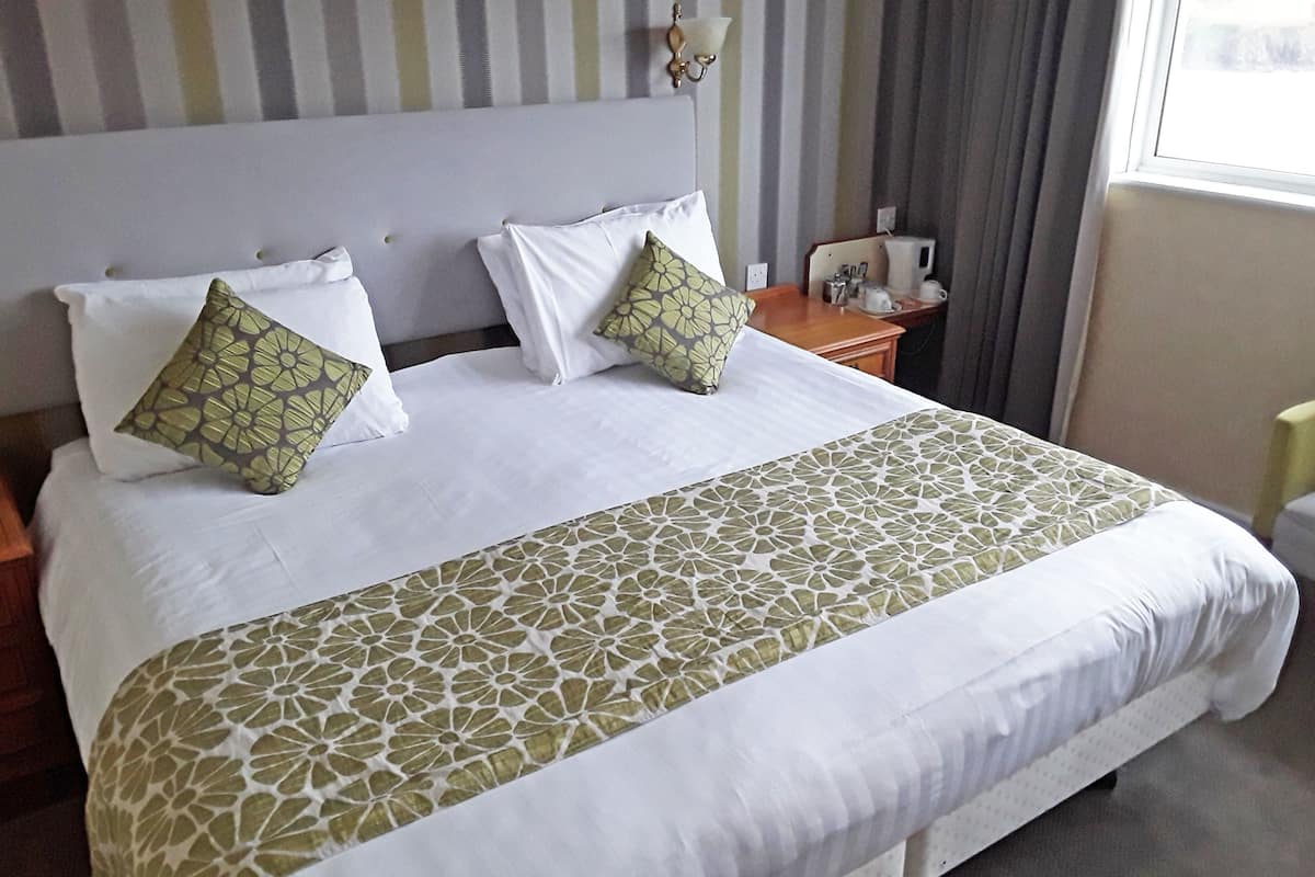 A neatly made bed with white linens and decorative pillows, a bedside table with a lamp, and a window with curtains.