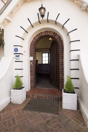 An entrance with a brick archway, a sign indicating a smoking area, and a small plant in a planter. - The Cottage Hotel (Kingsbridge)