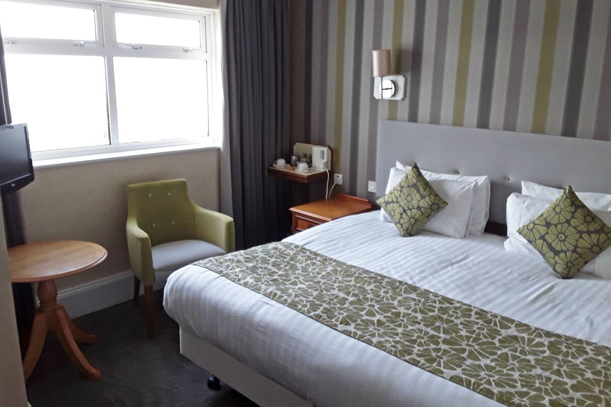 A hotel room with a bed, a chair, a small table, a TV, and a window.