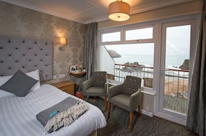 A hotel room with a bed, two armchairs, a desk, a lamp, and a view of the sea. - The Cottage Hotel (Kingsbridge)