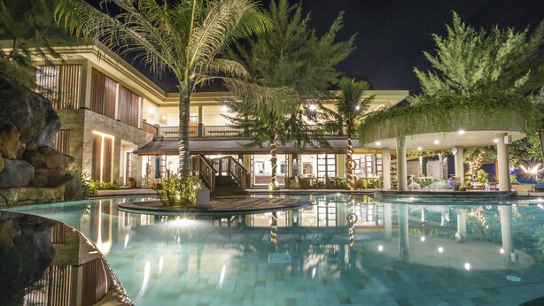 A nighttime view of a hotel pool area with a large pool, palm trees, and a well-lit outdoor seating area. - Akoya Pool Villa (Gili Trawangan)