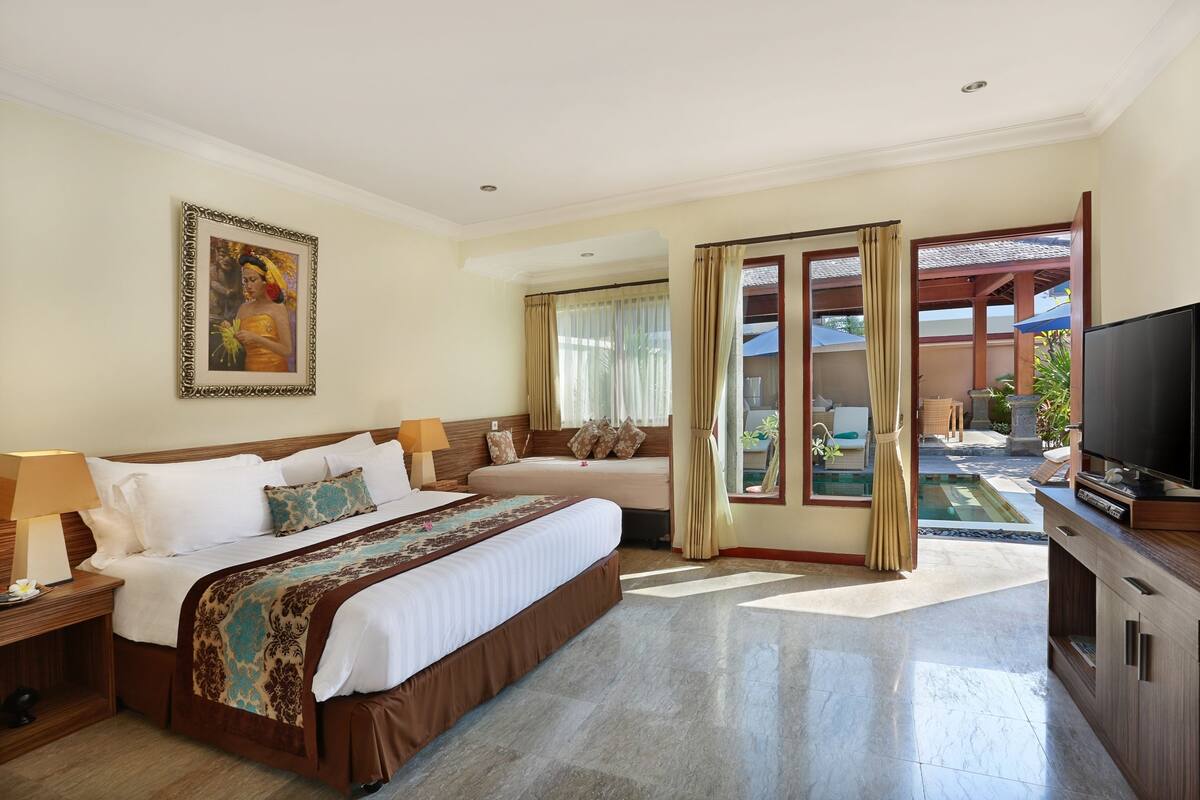 A hotel room with a large bed, a TV, and a view of the outdoor pool area.