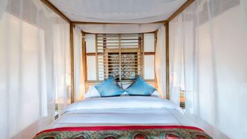 Una cama con sábanas blancas, almohadas azules y una colcha estampada, además de un cabecero de madera.