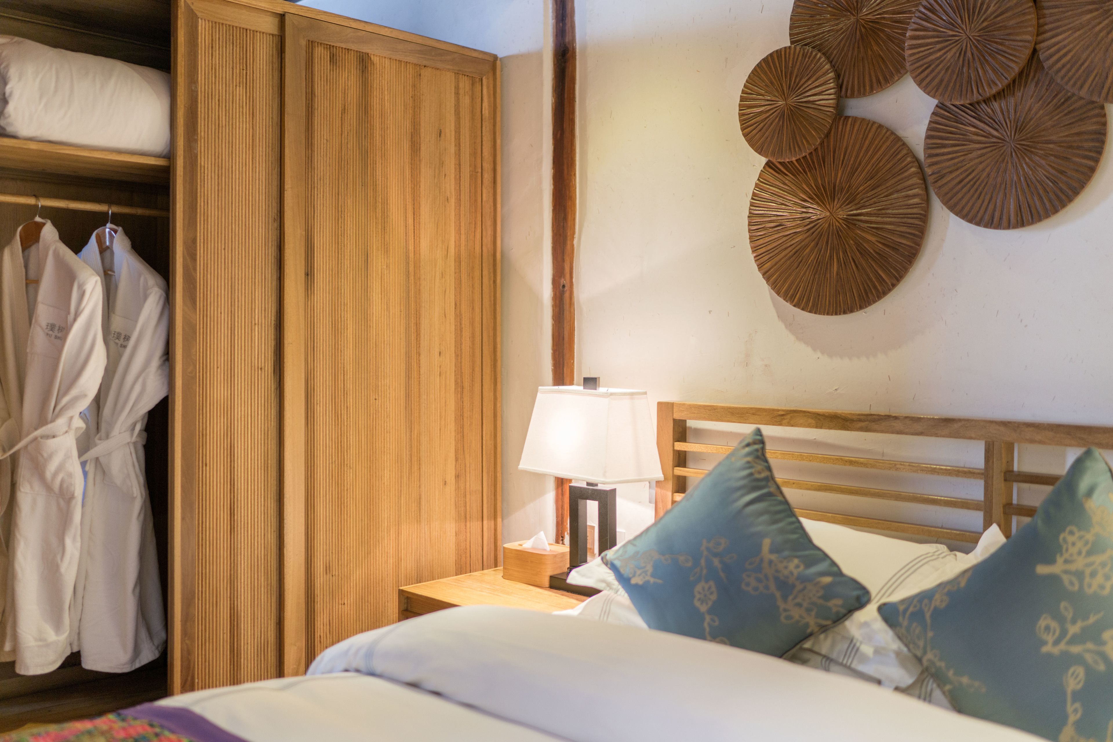 Un dormitorio ordenado con un armario de madera, una mesita de noche con lámpara y decoración en la pared.