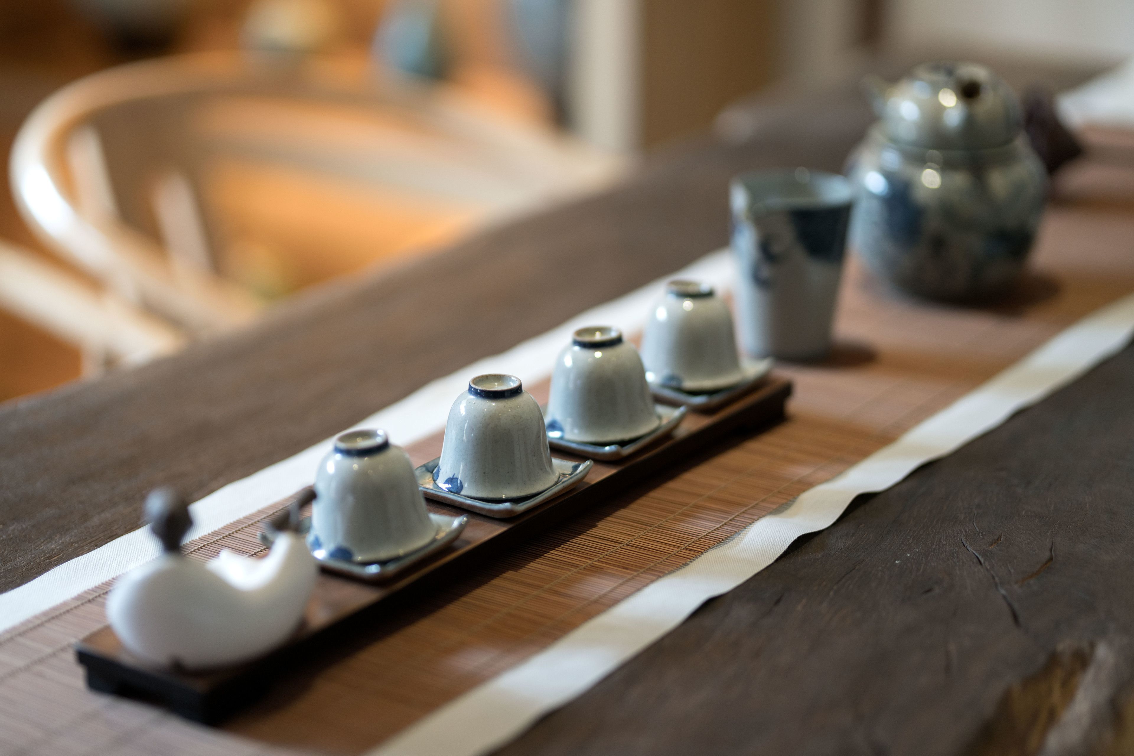 A wooden table with a series of white teapots and a teapot on a tray.